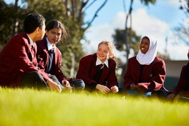 Students sit on the grass in their school uniform while talking